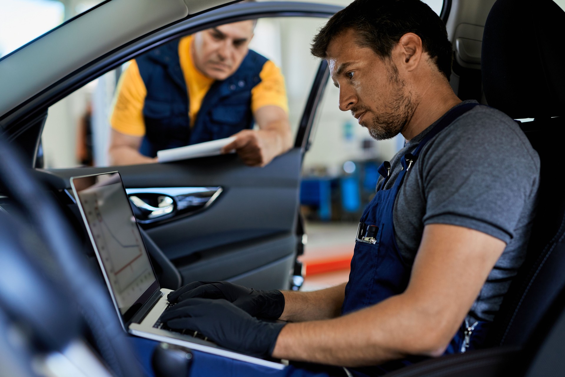 Locksmith checking car performance while running diagnostic on laptop in a workshop.