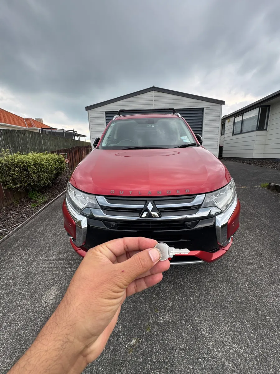 Roof rack key held up in front of a red Mitsubishi Outlander with roof bars fitted