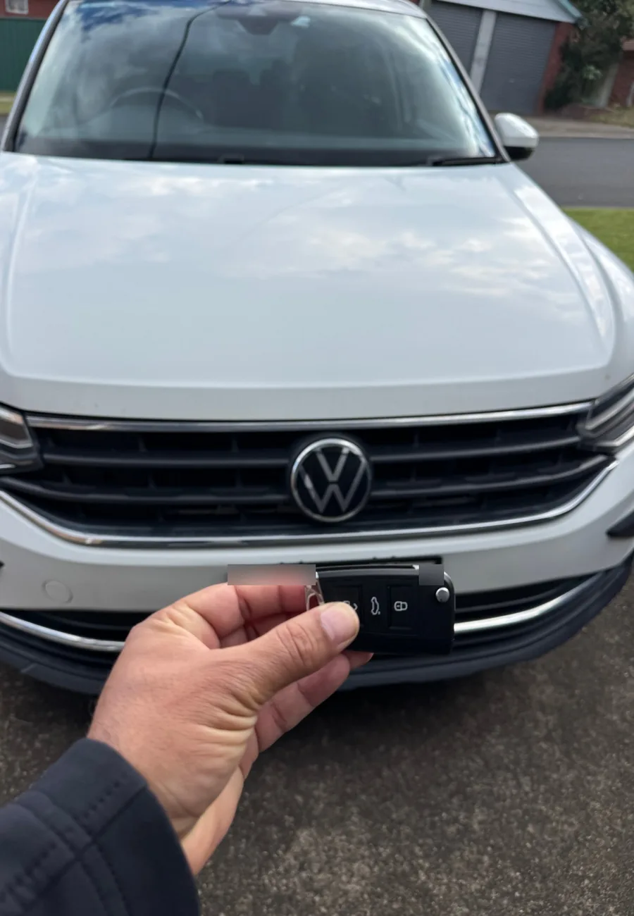 New VW flip key held up in front of a white Tiguan